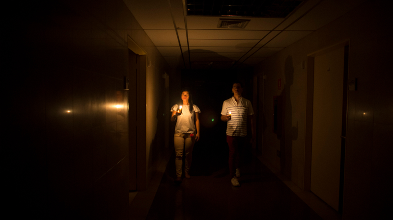 Relatives of a patient use candles to navigate a darkened clinic in Caracas on March 7, 2019.